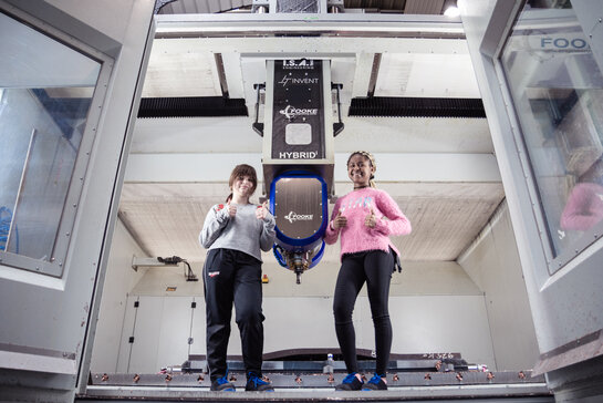 Zwei Schülerinnen stehen neben eine Maschine und haben den Daumen hoch